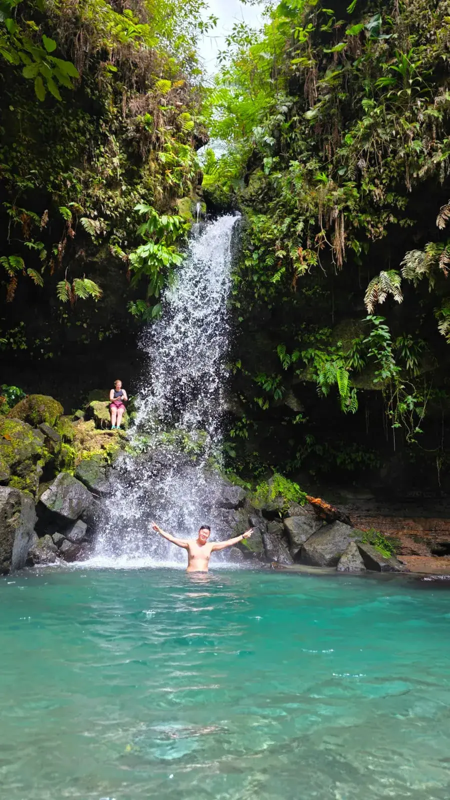Guest standing beneath a tall rainforest waterfall